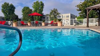 A pool with red chairs and a red umbrella.